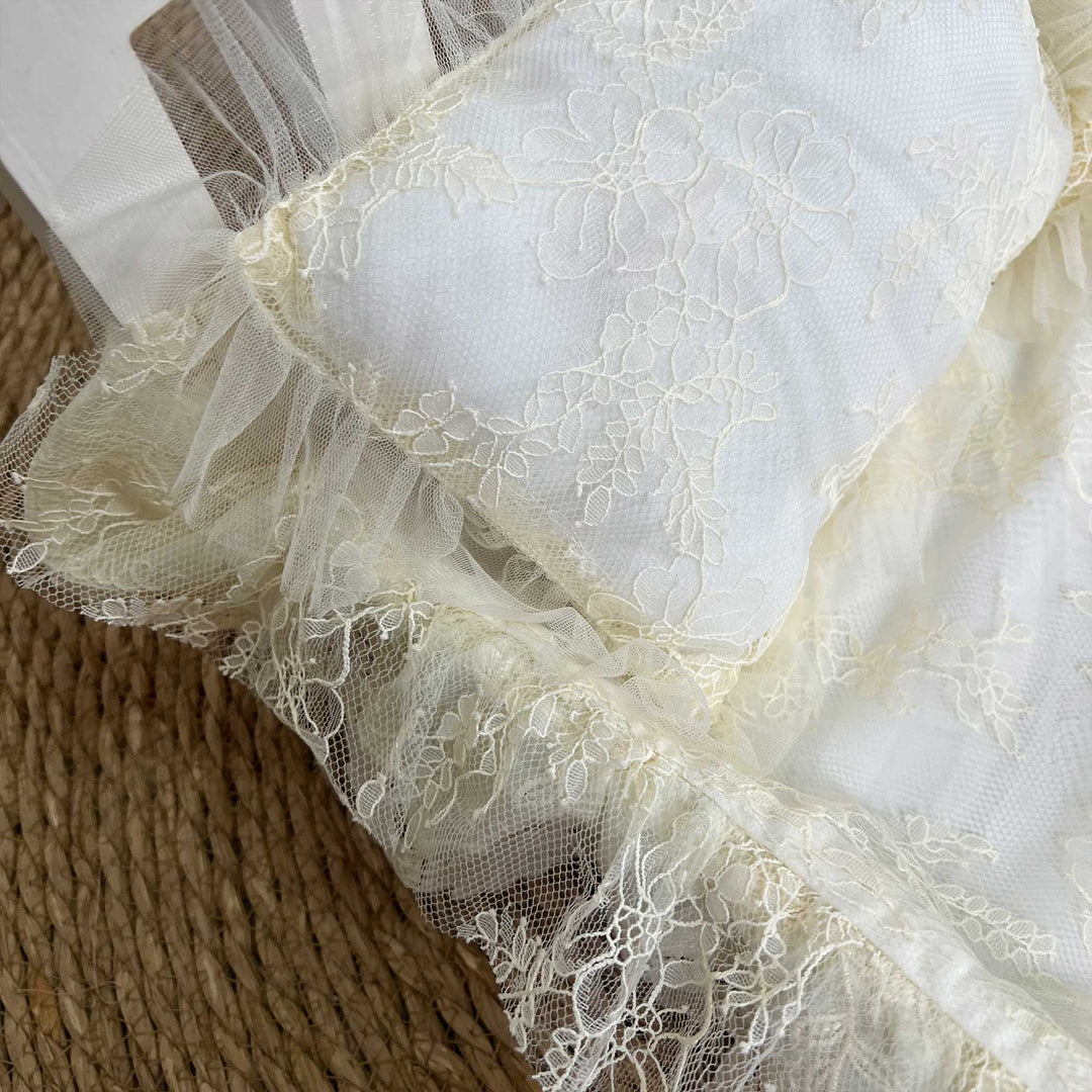 A close-up view of a beige lace set featuring ruffled tulle trim.