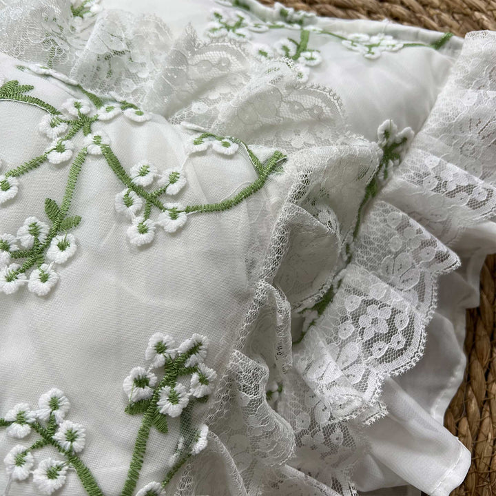 A close-up view of a green floral embroidery pillow featuring ruffled lace trim.