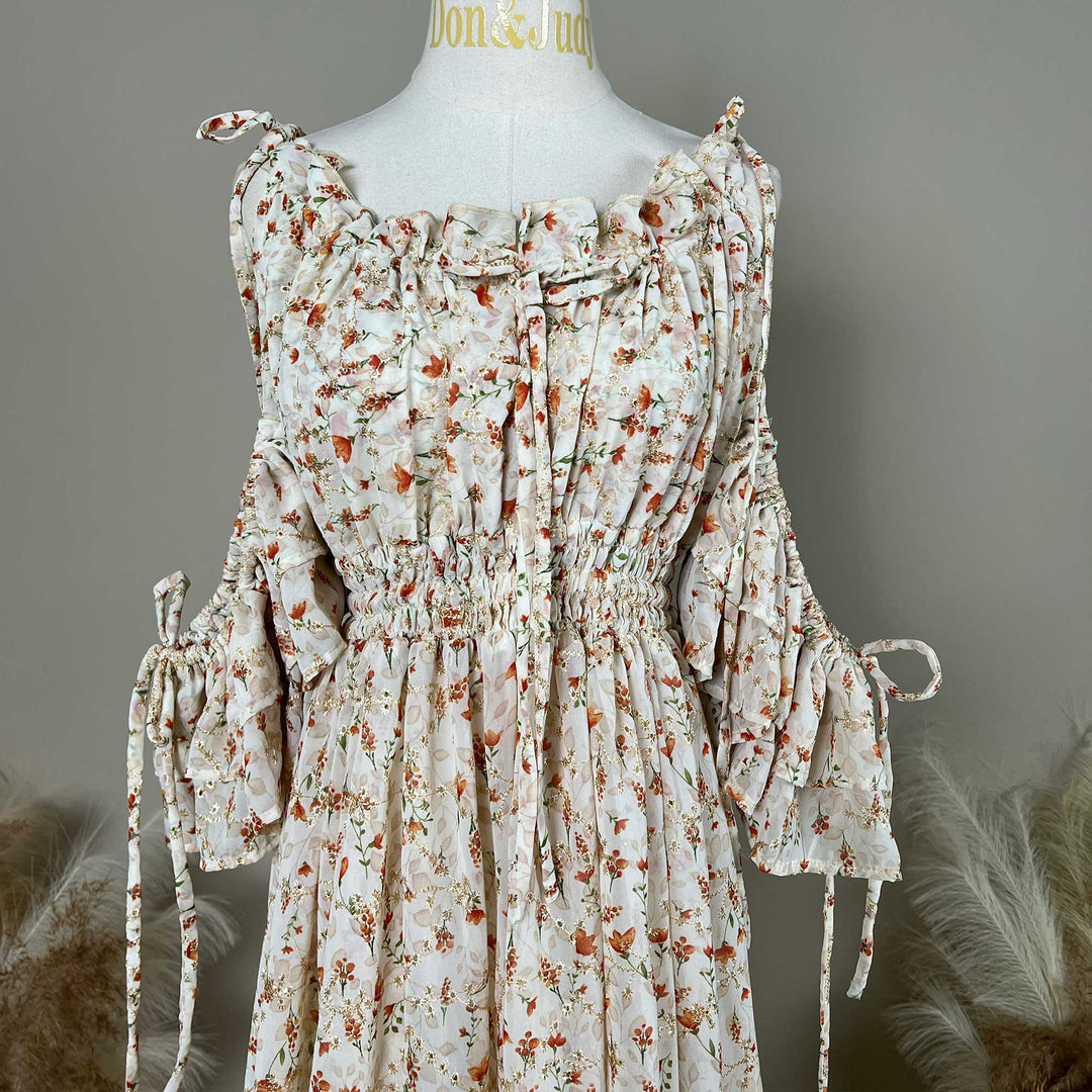 A mannequin displays an Alke orange floral dress featuring ruching and strings at the neckline and waist.