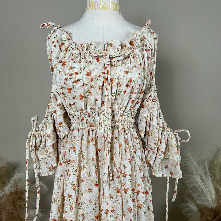 A mannequin displays an Alke orange floral dress featuring ruching and strings at the neckline and waist.