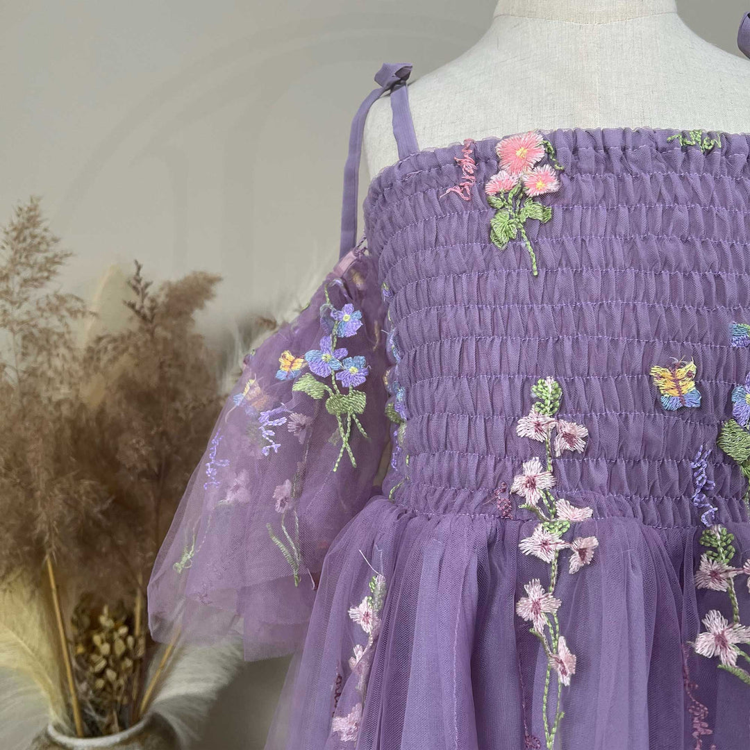 A close up of a mannequin displays an Ananke purple floral embroidered dress.