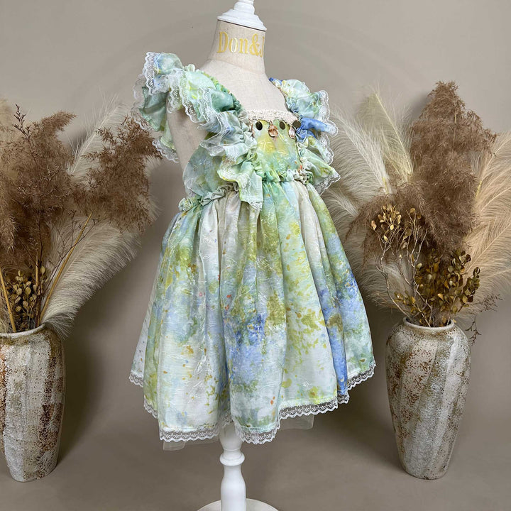 A side view of a mannequin displays a tie dye chiffon dress with ruffles. 