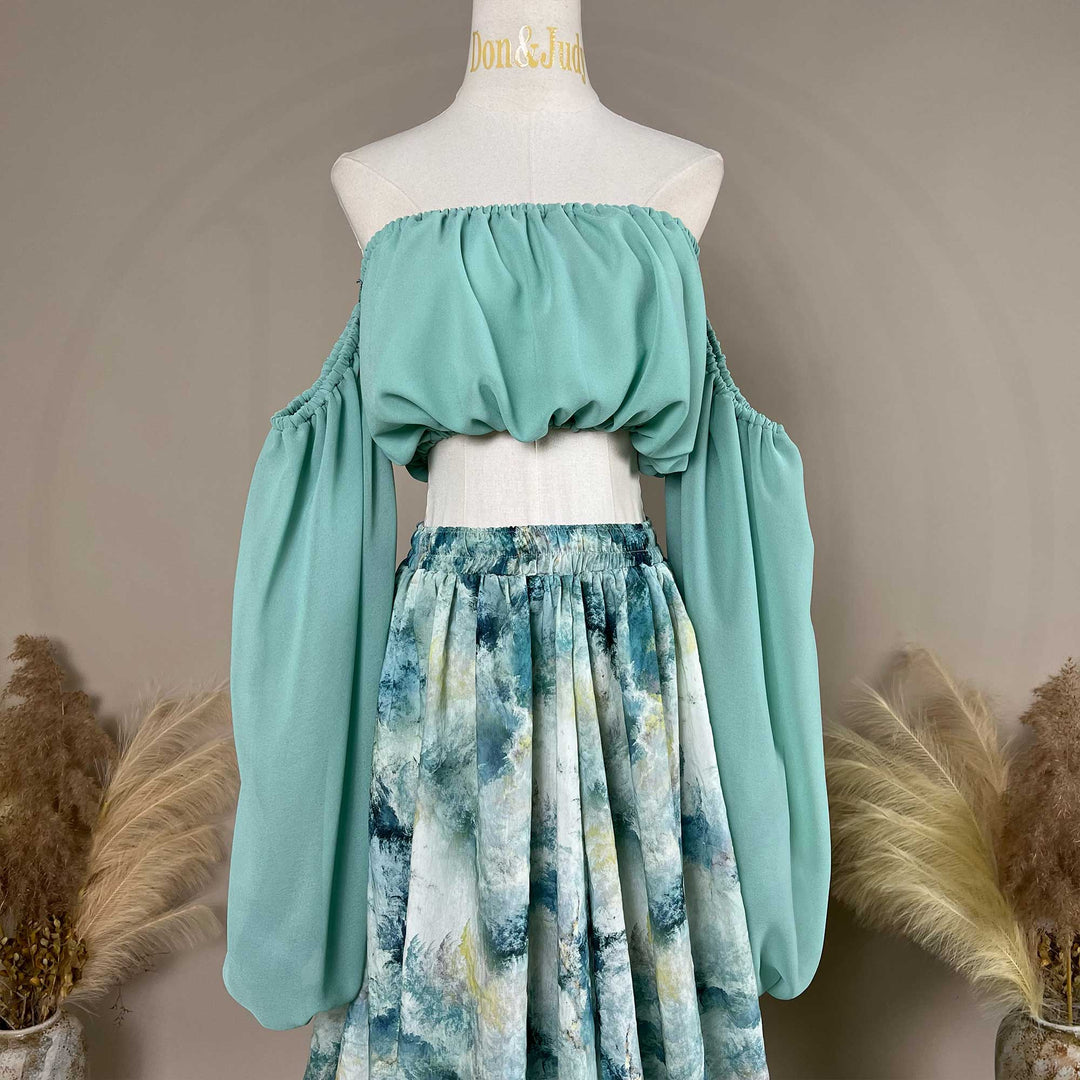 A close up of a Alala mint off shoulder top and a tie dye printed maxi skirt with a train are displayed on a mannequin. 