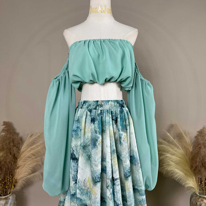 A close up of a Alala mint off shoulder top and a tie dye printed maxi skirt with a train are displayed on a mannequin. 