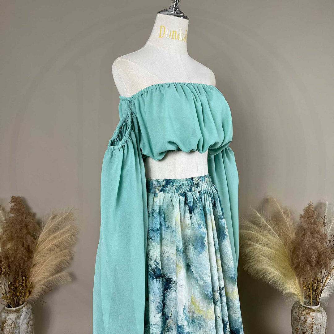 A close up of a Alala mint off shoulder top and a tie dye printed maxi skirt with a train are displayed on a mannequin. 