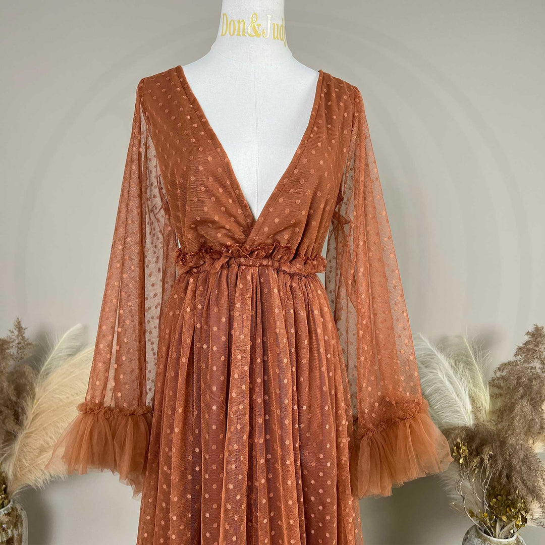 A terracotta polka dot tulle maternity dress is displayed on a mannequin torso. The dress features a V-neckline, long sheer sleeves with ruffled cuffs, and a gathered waist with ruffle detailing.