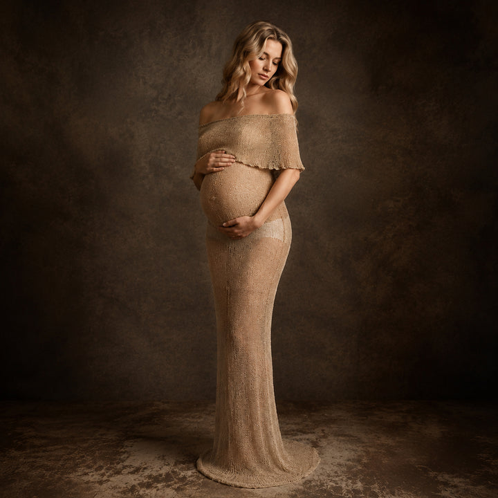 A pregnant woman in an Aletheia camel sparkling off-shoulder gown stands holding her belly.