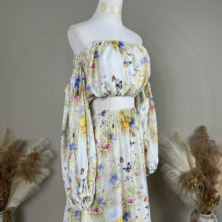 A side view of an Aphaea floral and butterfly print off-shoulder two-piece is displayed on a mannequin.