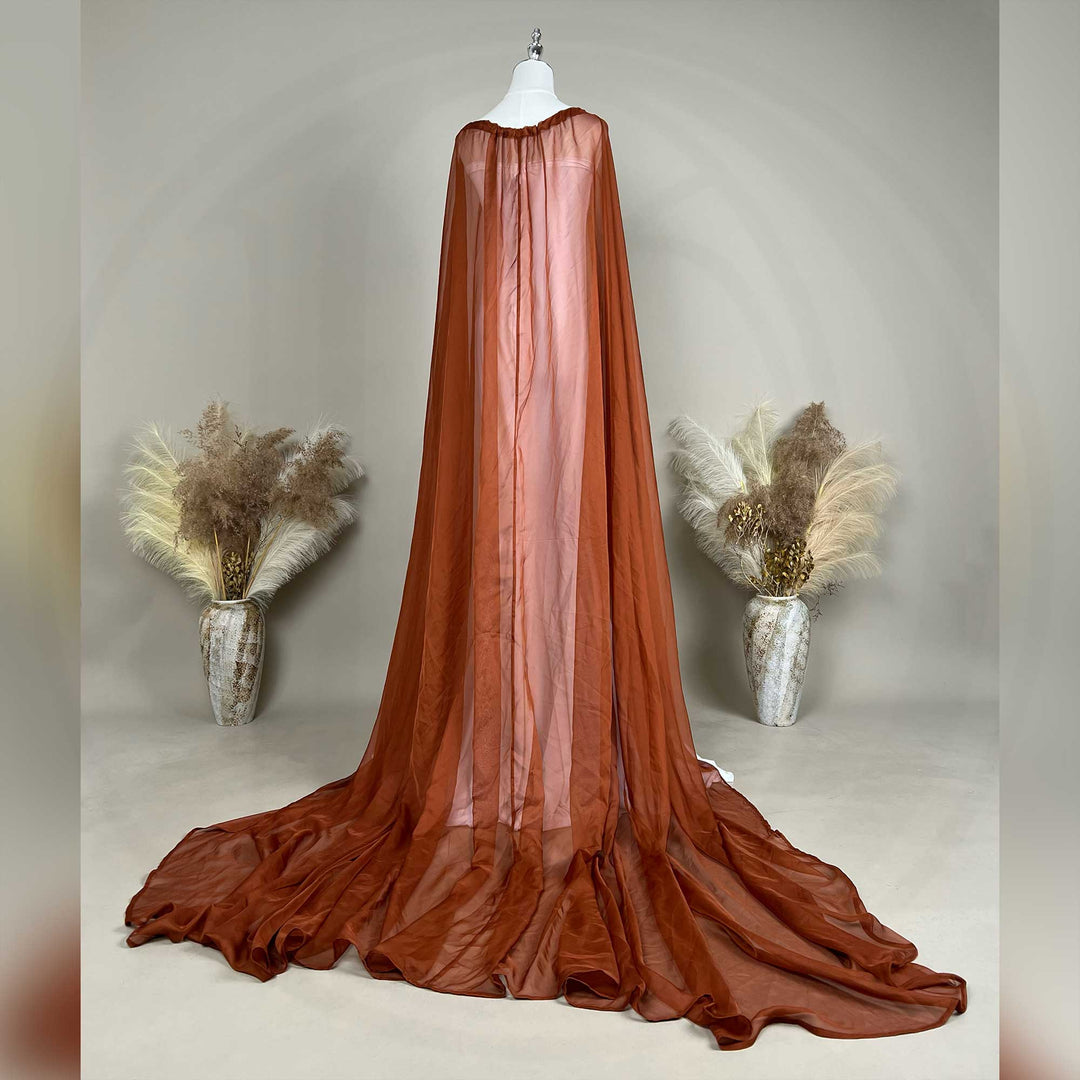 A back view of an Astraea satin maxi cape maternity dress with a terracotta chiffon cape is displayed on a mannequin.