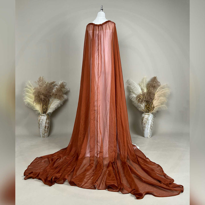 A back view of an Astraea satin maxi cape maternity dress with a terracotta chiffon cape is displayed on a mannequin.