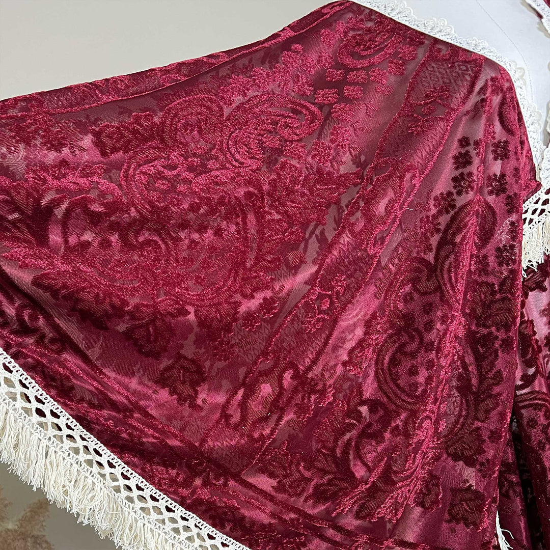A red wine sheer cape with embroidered paisley patterns is displayed. White lace trim with tassels decorates the edges.