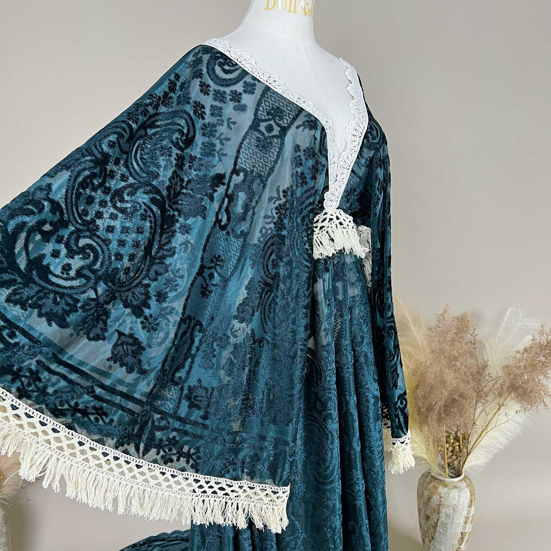 A green sheer cape with embroidered paisley patterns is displayed. White lace trim with tassels decorates the edges.