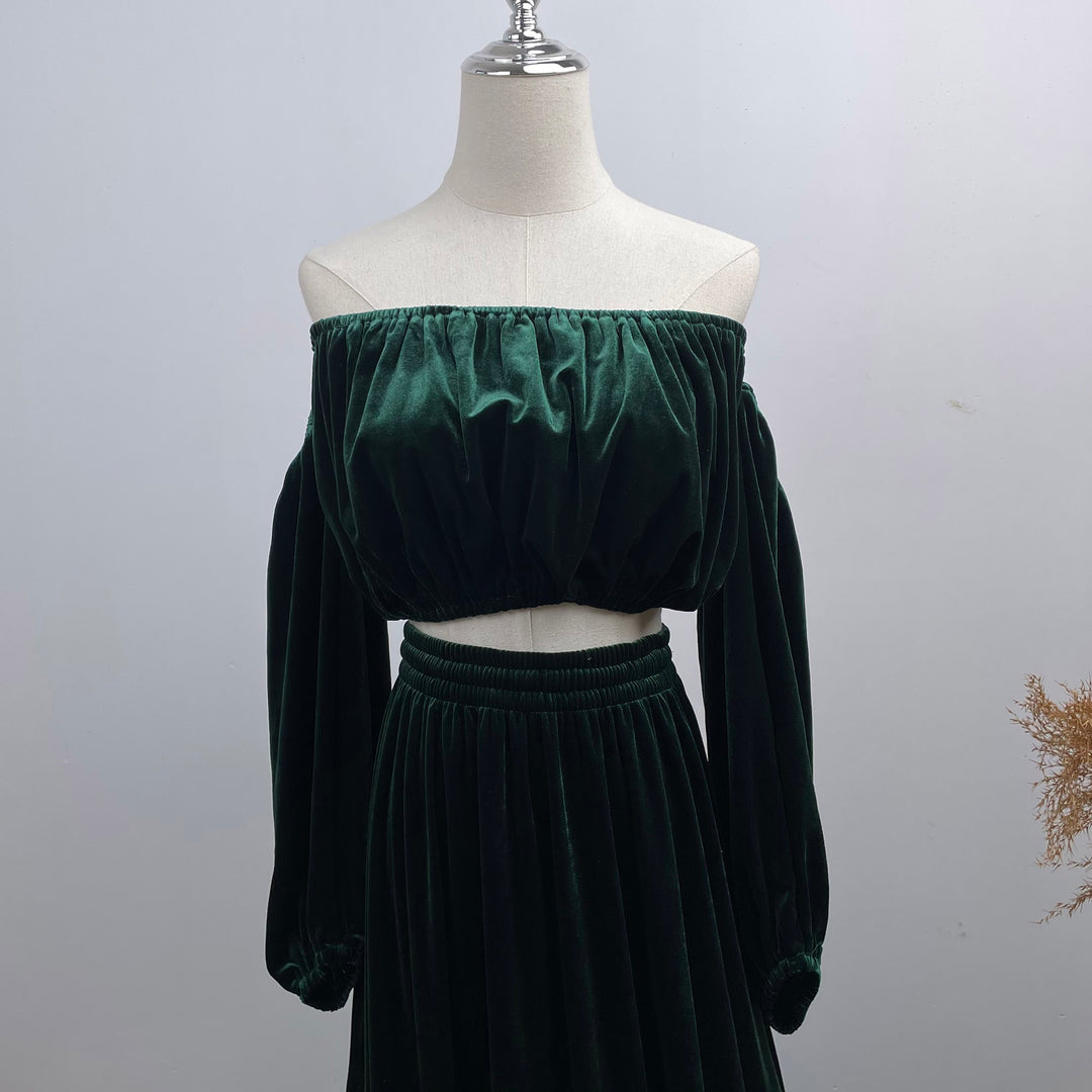 A dark green velvet off-the-shoulder two-piece set consisting of a cropped long-sleeve top and a matching high-waisted skirt, displayed on a cream dress form mannequin against a light gray background.