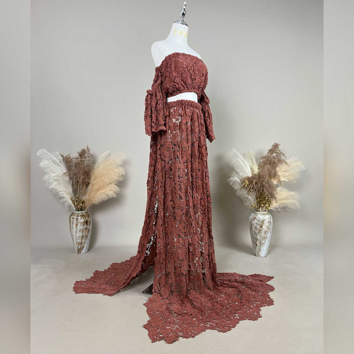 A terracotta two-piece lace maternity set displayed on a mannequin, featuring an off the shoulder ruffled crop top and a high waisted floor length skirt with a sweeping train.