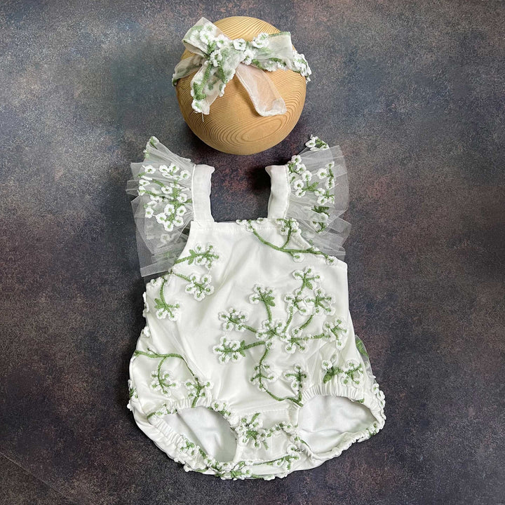 A romper laid flat from the front, showing the square neckline, tulle flower straps on both sides and gathered leg openings, with the same headband above.