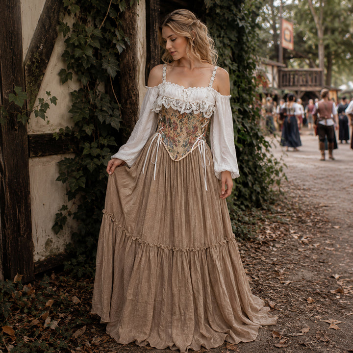 A woman stands outdoors by a stone wall wearing a Brigid ivory off-shoulder top, floral corset, and khaki skirt.