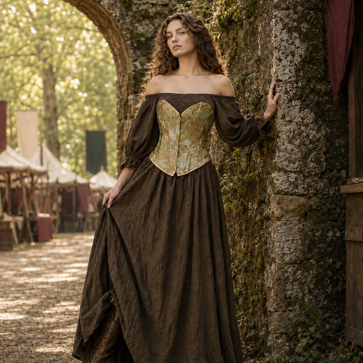 A woman stands by a stone arch outdoors wearing a Brimo khaki off-shoulder gown and green floral corset. Trees, tents, and market stalls are visible in the background.