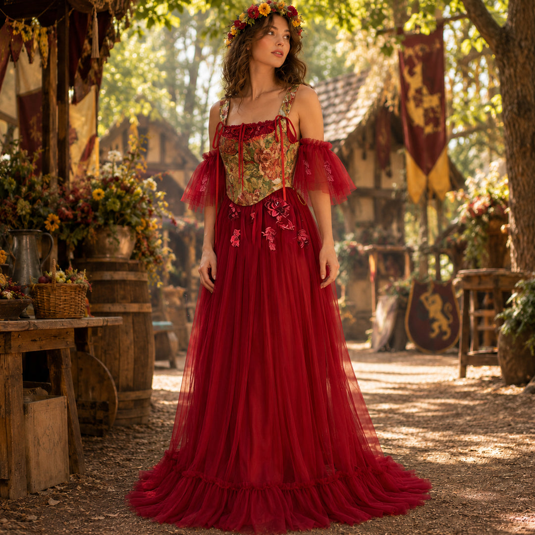 A woman wearing a Cailleach flower crown, red tulle gown, and floral corset stands in an outdoor medieval setting. Wooden houses, flags, and barrels with flowers are in the background.
