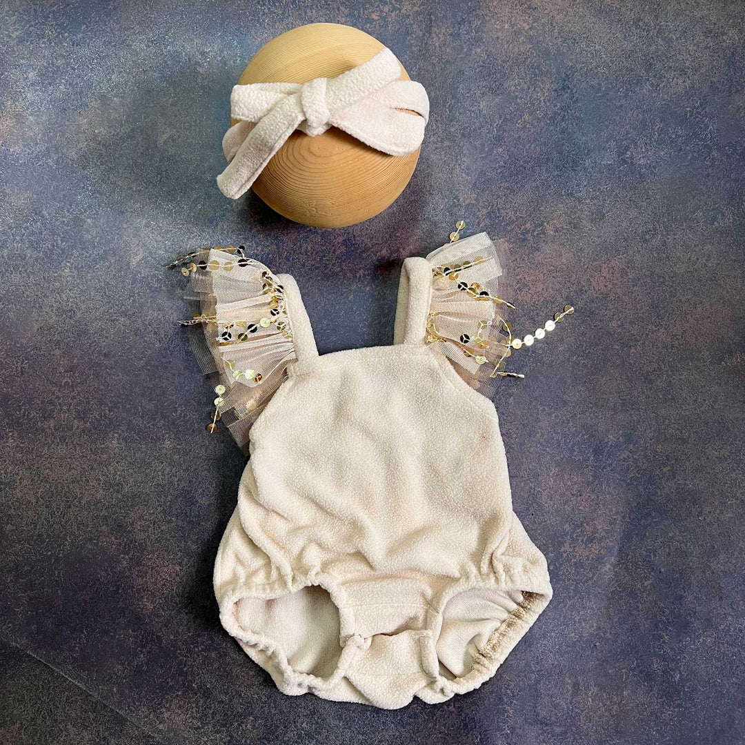 A romper laid flat from the front, showing the square neckline, tulle sequin straps on both sides and gathered leg openings, with the same bow headband above.
