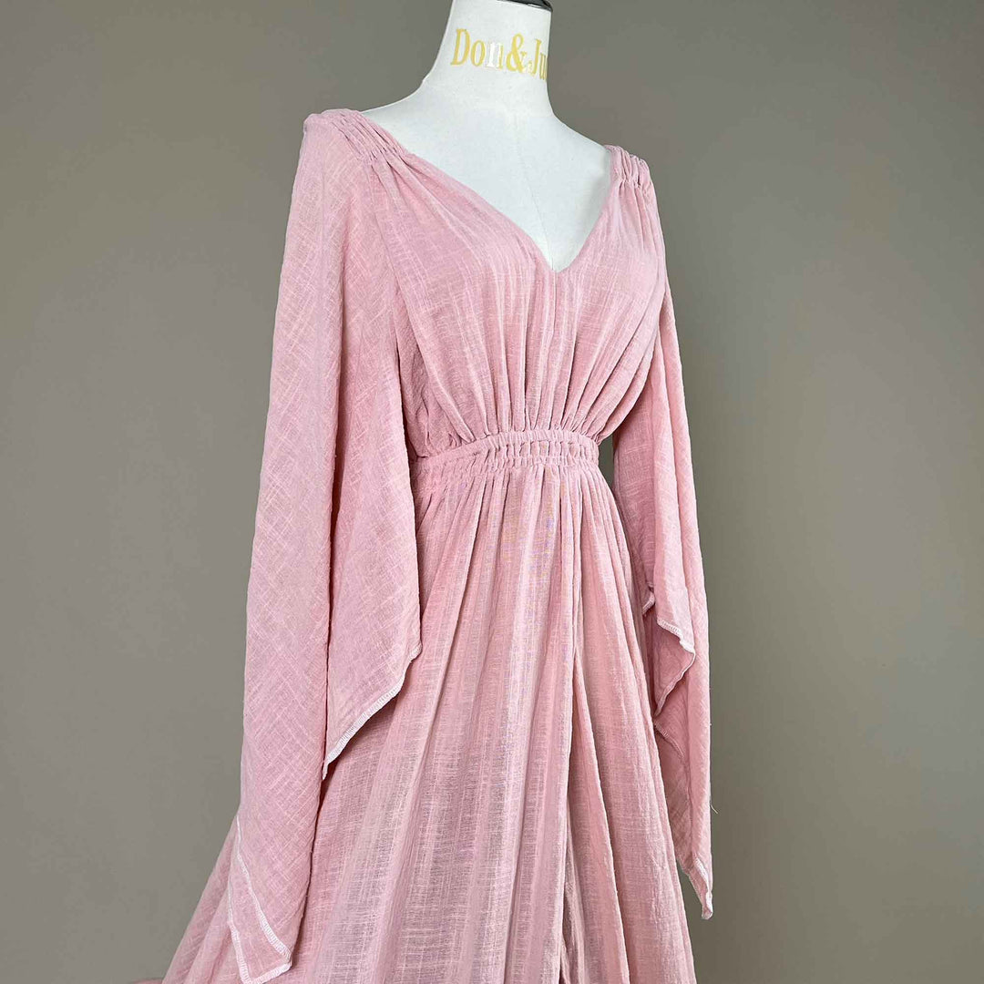 Close up of a Daphne Pink long-sleeved V-neck gown is displayed on a mannequin.The dress features a high front slit and its hem and train are spread out on the wooden floor.