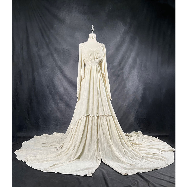 A Daphne light grey long-sleeved V-neck gown is displayed on a mannequin, with hands positioned on the simulated belly. The dress features a high front slit and its hem and train are spread out on the wooden floor.

