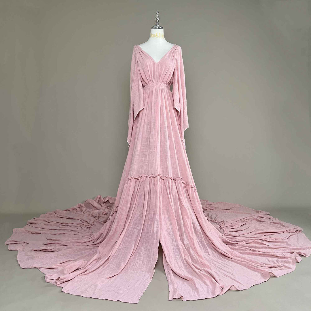 A Daphne Pink long-sleeved V-neck gown is displayed on a mannequin.The dress features a high front slit and its hem and train are spread out on the wooden floor.