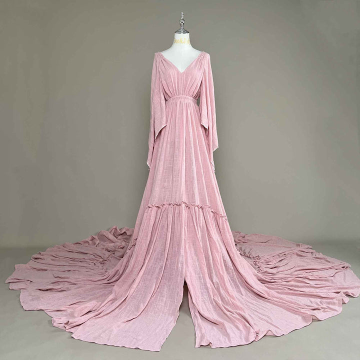 A Daphne Pink long-sleeved V-neck gown is displayed on a mannequin.The dress features a high front slit and its hem and train are spread out on the wooden floor.