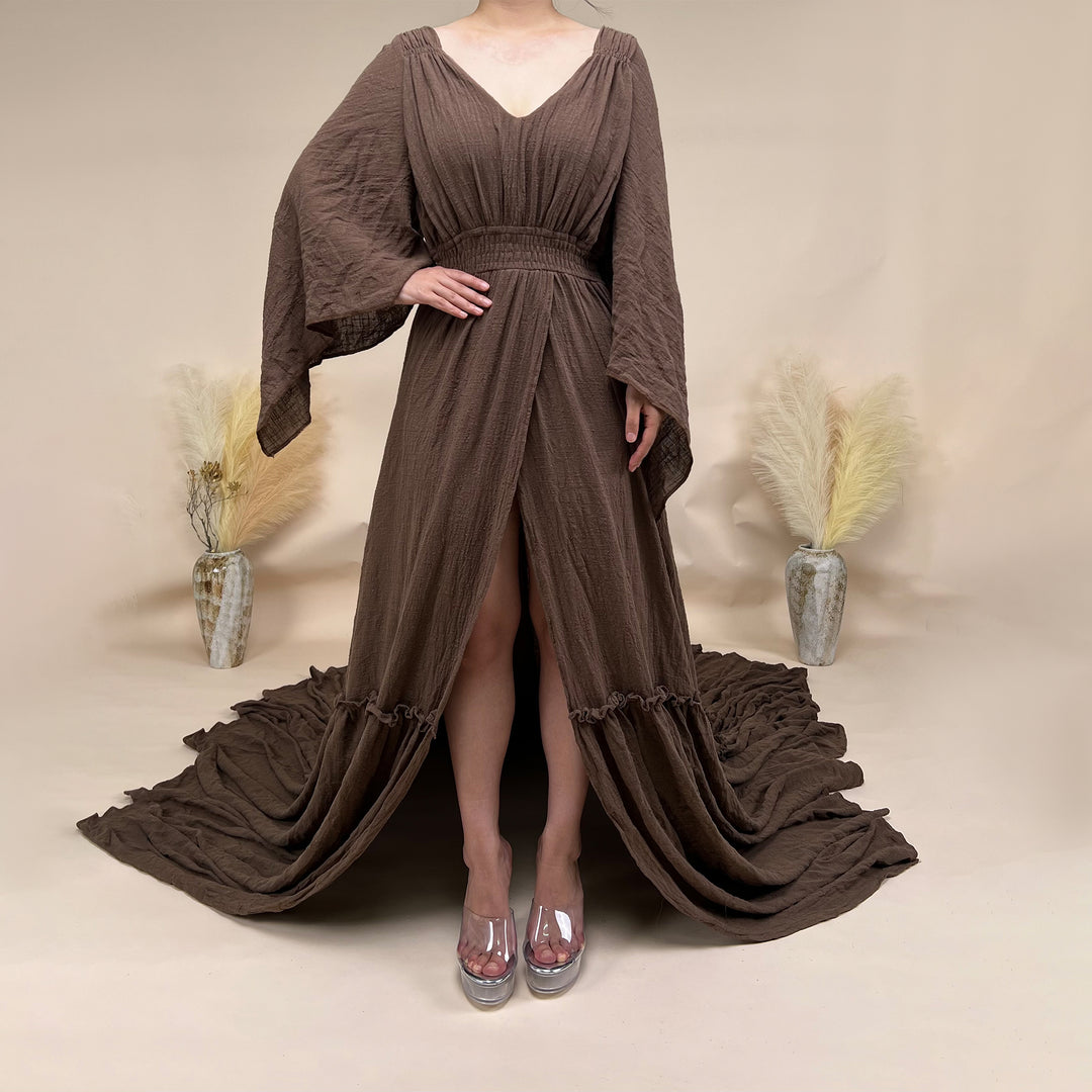 A Daphne coffee long-sleeved V-neck gown is displayed on a mannequin. The dress features a high front slit and its hem and train are spread out on the wooden floor.

