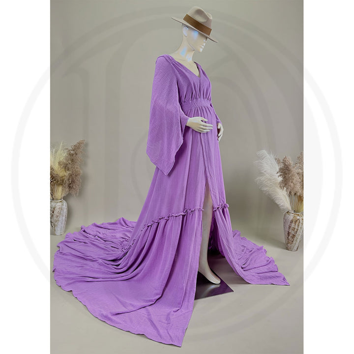 A Daphne lavender long-sleeved V-neck gown is displayed on a mannequin, with hands positioned on the simulated belly. The dress features a high front slit and its hem and train are spread out on the wooden floor.