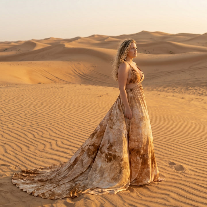 A woman stands in the desert wearing a Demeter tie dye printed spaghetti strape two-piece gown with a train. 