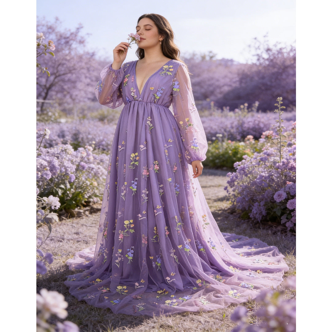 A woman smells a flower in a field, wearing a Dike purple tulle long-sleeve gown with floral embroidery and a train.