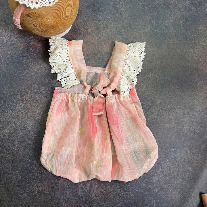 the back of a romper laid flat, straps tied at the chest, gathered waist, part of the headband visible at the upper left.