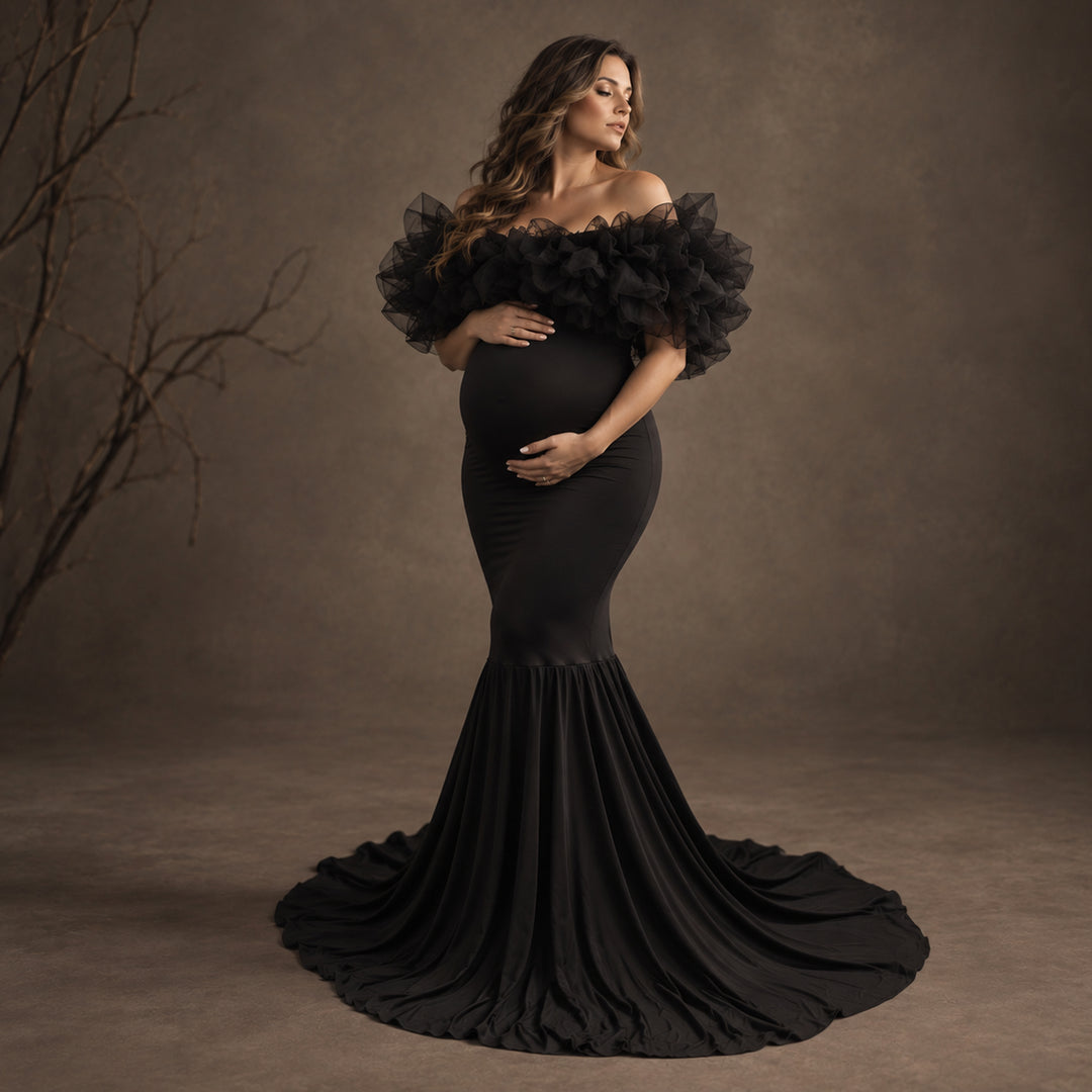 A pregnant model wearing a black off-the-shoulder maternity gown with dramatic ruffled sleeves and a mermaid-style fitted silhouette.
