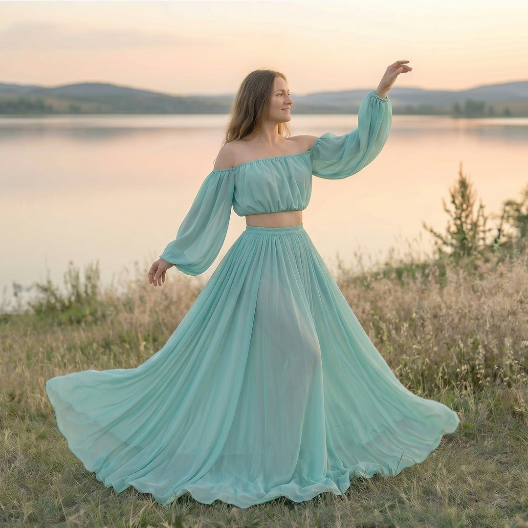 A woman stands in a grassy field wearing a Gaia mint flowy chiffon off-shoulder dress.