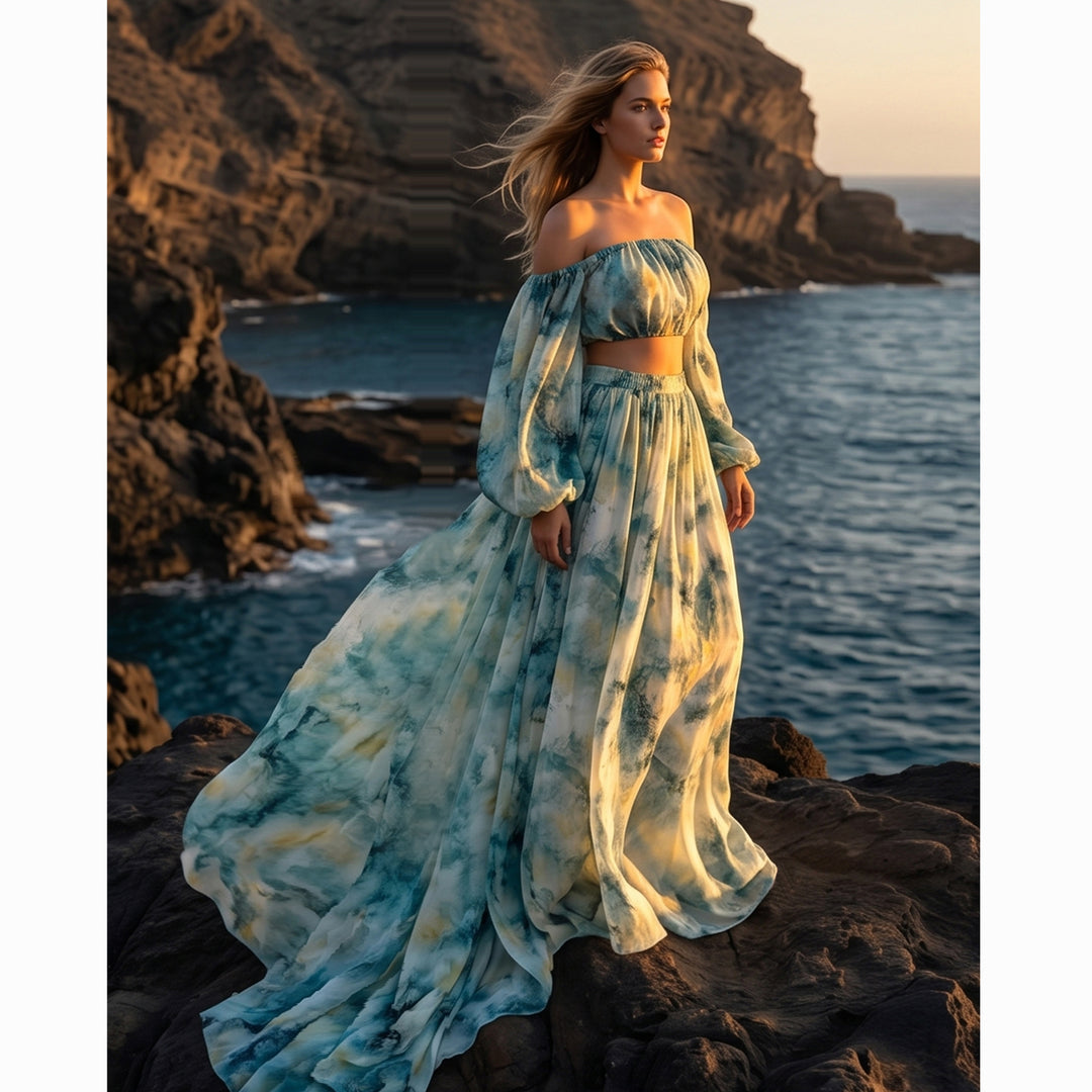 A woman in a Hestia tie dye off shoulder crop top and maxi skirt stands on rocky cliffs by the ocean.