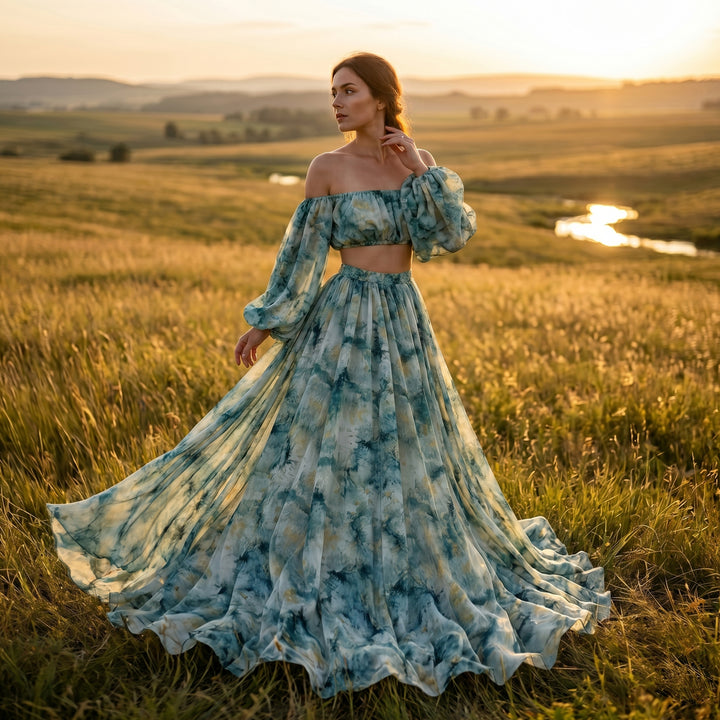 A woman stands in a field wearing a Hestia tie dye print two-piece dress with a long skirt. 