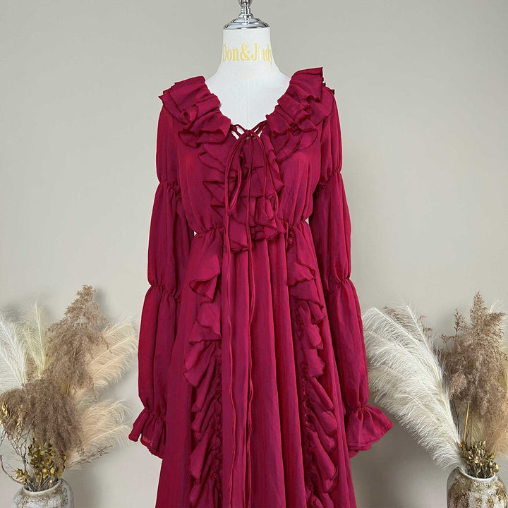 A red Kallectoria dress with dramatic ruffles and long sleeves, displayed on a white mannequin torso. The dress features a tie-front neckline and gathered waist details.