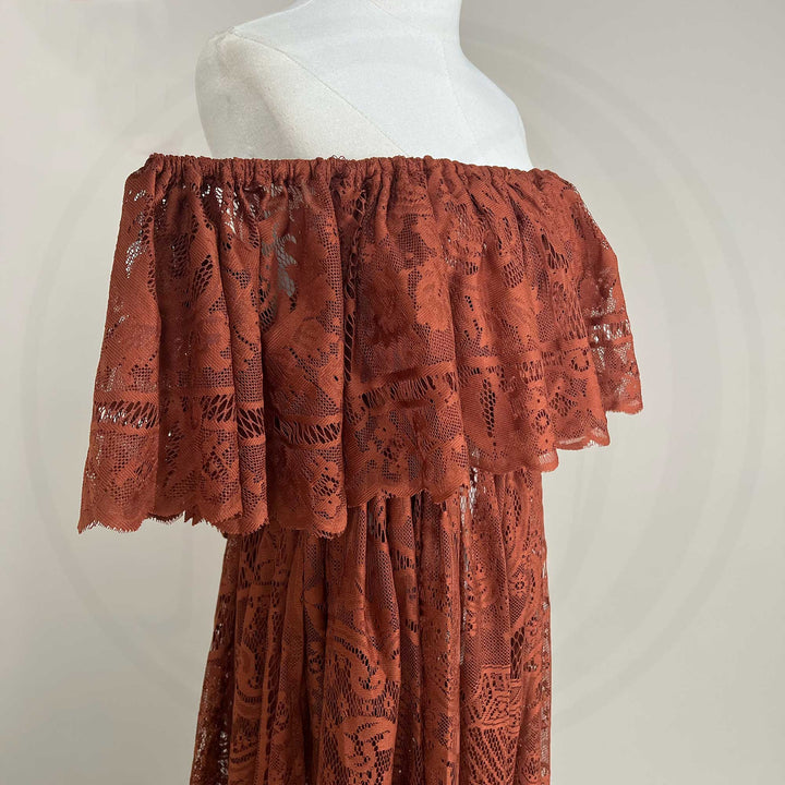 A mannequin a close-up of a terracotta off-shoulder lace dress with a ruched neckline and tiered sleeves; the fabric features an openwork pattern.