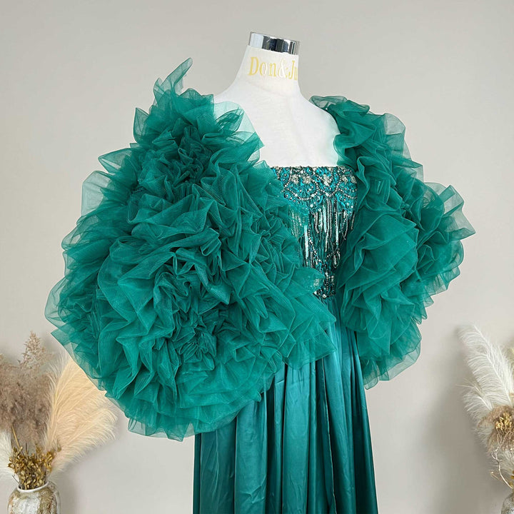 A green Luna ruffled shawl is displayed on a mannequin .The shawl is made of ruffled fabric and covers the mannequin's shoulder and arm areas.