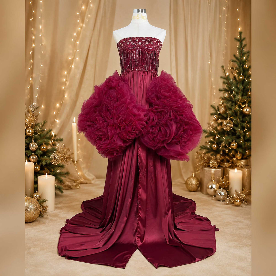 A red Luna strapless gown is displayed on a mannequin, featuring ruffled designs at the waist. The background includes Christmas trees, candles, and string lights.
