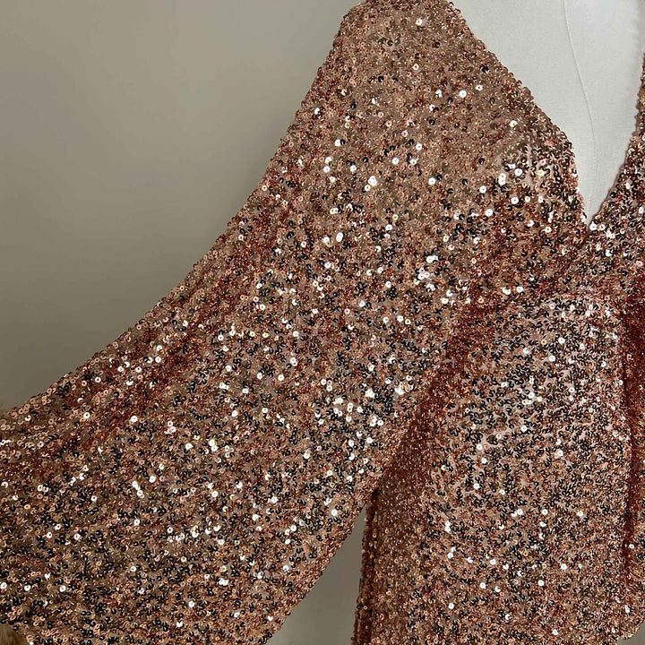 A pink gold Mara dress sequined gown, featuring a V-neck and flared sleeves displayed on a mannequin.