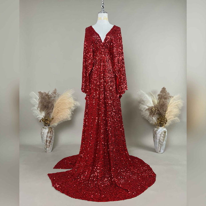 A Mara red sequined gown is displayed on a mannequin, featuring a V-neck and flared sleeves. The hem trails on the floor.