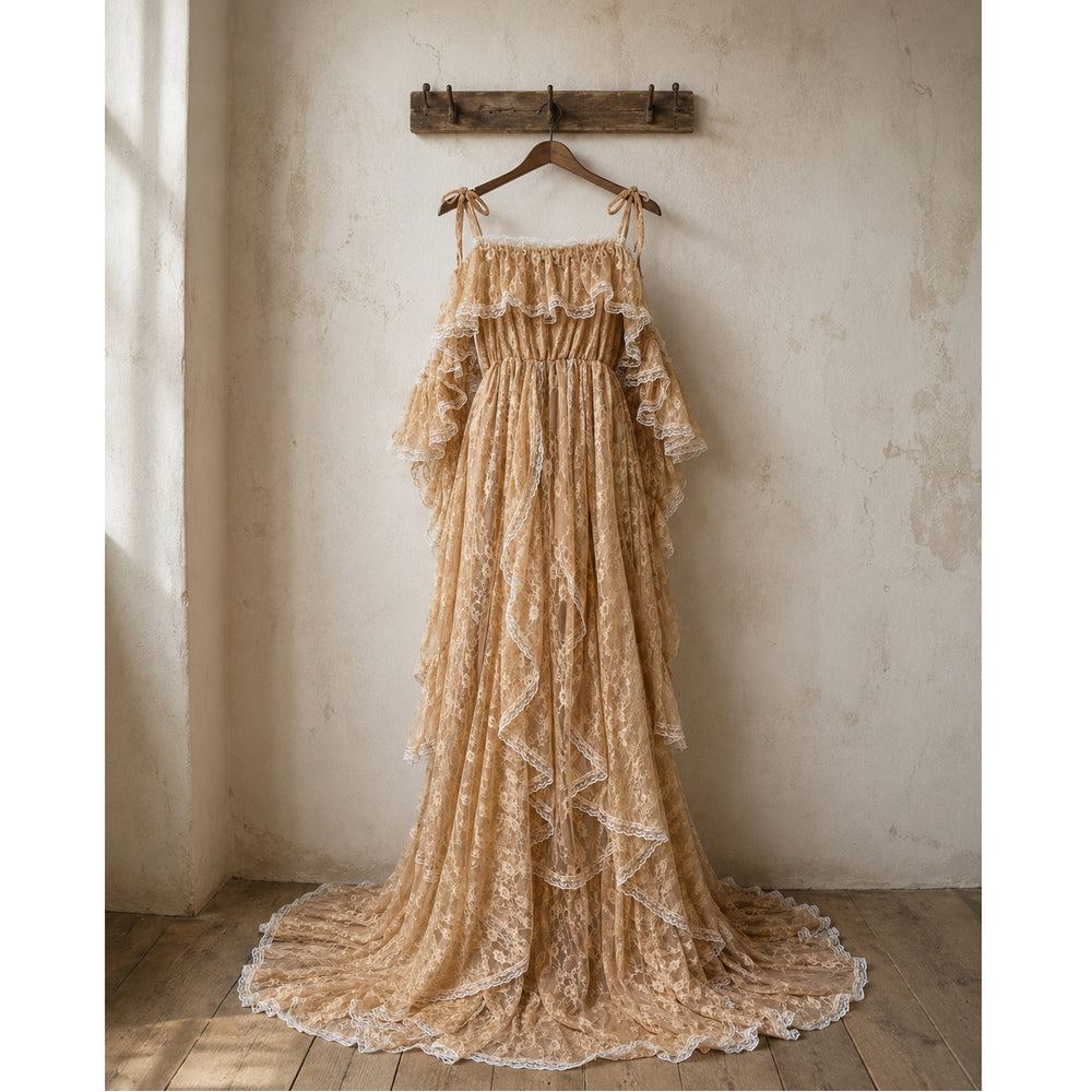 A Melinoe khaki lace tiered ruffle off-shoulder maternity photography dress hangs on a rustic wooden hanger against a textured, light beige wall. 