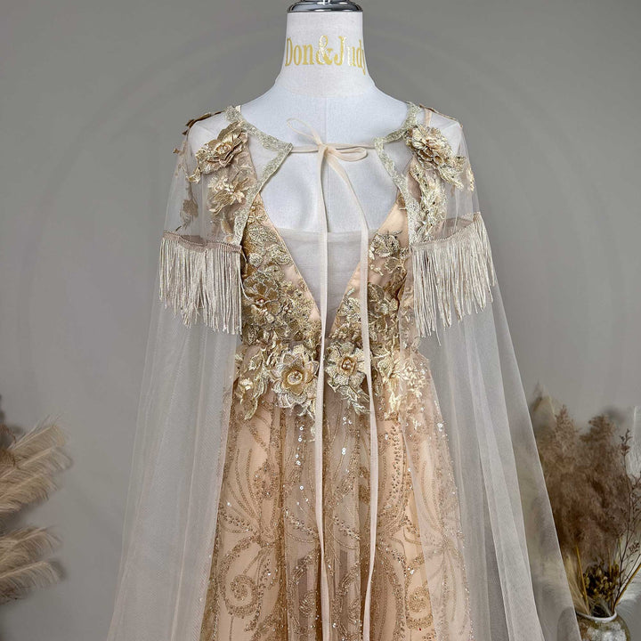 A mannequin displays a Pandia gold sequined gown with a tulle cape, featuring 3D floral decorations and fringe cuffs.