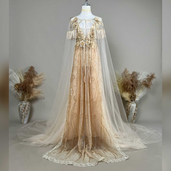 A gold sequined gown with a Pandia tulle cape is displayed on a mannequin, featuring fringe cuffs and a train skirt.