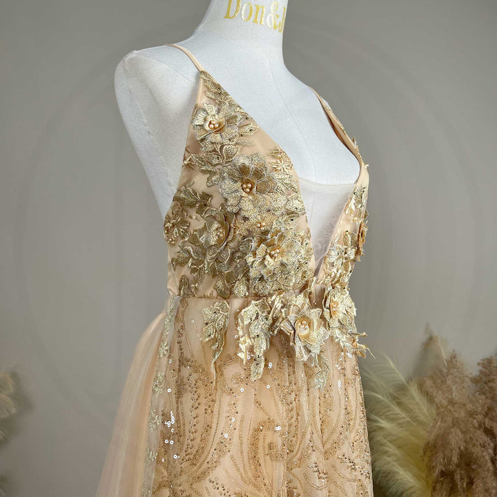 A mannequin displays the upper body of a Pandia gold spaghetti strap gown with a deep V-neck and 3D floral decorations.