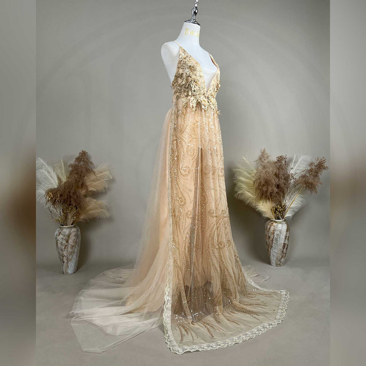 A mannequin displays a Pandia gold sequined spaghetti strap gown with a deep V-neck, 3D floral decorations, and a train skirt.